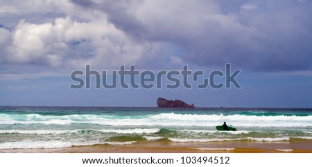 Picture a beautiful beach where a tidal wave that are coming to some surfers near the rocky island in Bretagne, Finistere, France.