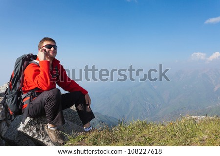 Image of a young man - a tourist, which sits on top and using a cell. In the background the snowy mountain tops of the clouds. Tibet in the Himalayas.