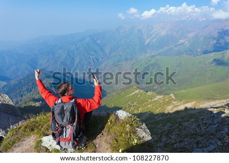 Image of a young man - a tourist, which sits on top and trying to use a cell. In the background the snowy mountain tops of the clouds. Tibet in the Himalayas.