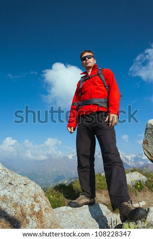 Image of a young man - a tourist, standing on top and looks at the camera. In the background the snowy mountain tops of the clouds. Tibet in the Himalayas.