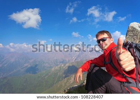 Image of a young man - a tourist, which sits on top and looks into the camera. In the background the snowy mountain tops of the clouds. Tibet in the Himalayas.
