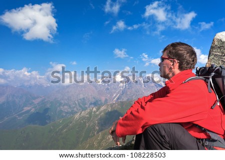 Image of a young man - a tourist, which sits on top and looks into the mountains. In the background the snowy mountain tops of the clouds. Tibet in the Himalayas.