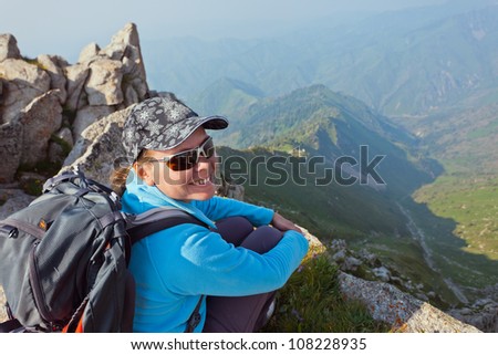 Image of a young woman - a tourist, which sits on top and looks into the camera. In the background the snowy mountain tops of the clouds. Tibet in the Himalayas.