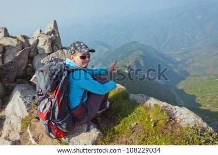 Image of a young woman - a tourist, which sits on top and looks into the camera. In the background the snowy mountain tops of the clouds. Tibet in the Himalayas.