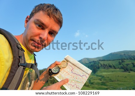 Picture of the tourist, who looks at the camera with map using a compass. In the background a beautiful valley with the tops of the mountains at sunset. Switzerland.