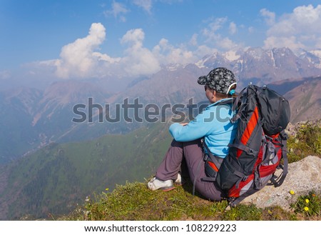 Image of a young woman - a tourist, which sits on top and looks into the maountains. In the background the snowy mountain tops of the clouds. Tibet in the Himalayas.