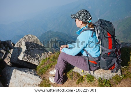 Image of a young woman - a tourist, which sits on top and looks into the maountains. In the background the snowy mountain tops of the clouds. Tibet in the Himalayas.