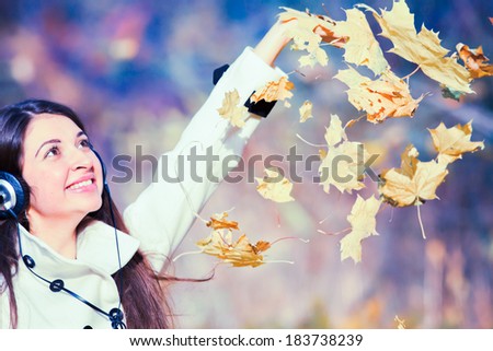 Young attractive woman with headphones enjoying music. Outdoors, autumn park