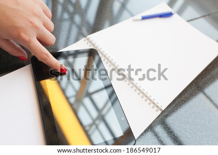 female finger touches the pc tablet, with background of copy space notebook and pen