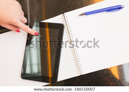 female finger touches the pc tablet, with background of copy space notebook and pen