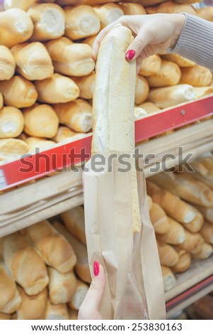 woman packs a French baguette in a plastic bag at supermarket