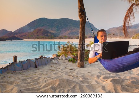 man uses laptop remotely at the beach