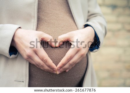 Pregnant woman outdoor, holding her hands on her stomach in the form of heart