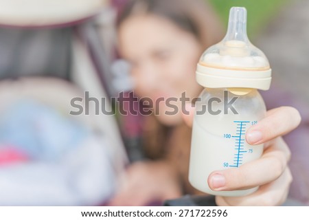 background of happy mom holding at hand baby bottle with milk at foreground