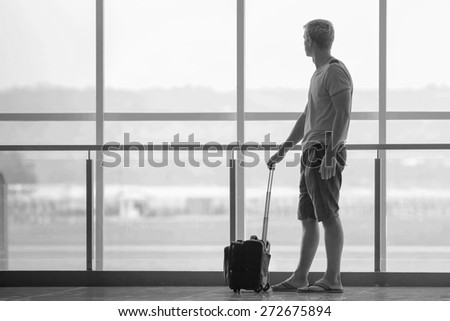 man with suitcase waiting a plane at terminal airport, he is looking at big window, black and white edition