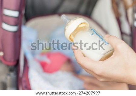 background of mom holding at hand baby bottle with milk at foreground