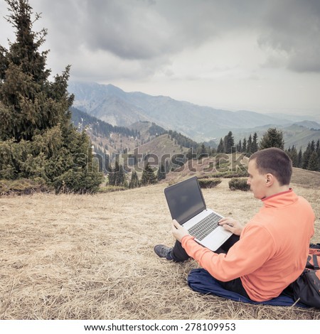 man dressed in red sweater uses laptop remotely with 3g or 4g network wireless at mountain, square orientation