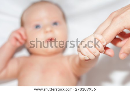 newborn baby holding her mother\'s finger, concept of love and mother care for kid, she lies on a white bed. It seems that the child is calling on the phone