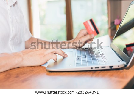 Concept of online payment by plastic card through the Internet Banking. Close-up of human hand for laptop and holding credit card, man is shopping indoor at home