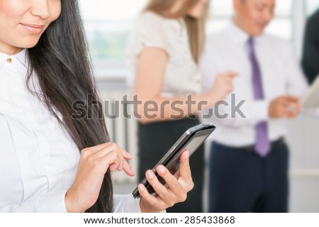 closeup image of successful asian business woman with magnificent long hair using mobile phone and business team at background. Image symbolizes corporation, company, uses new technology for success