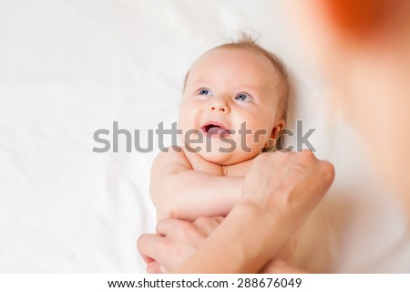 Mother makes massage and stretch for baby hands, with happy newborn at white bed, happy baby looking at copy space