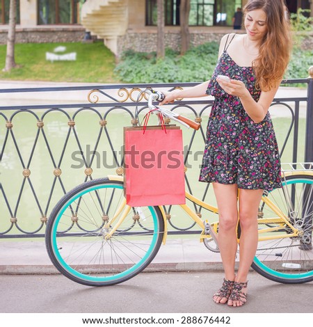 Pretty and happy caucasian woman with bugs using mobile phone or typing sms, near vintage bicycle. Her summer vacation in Europe for shopping and fun!