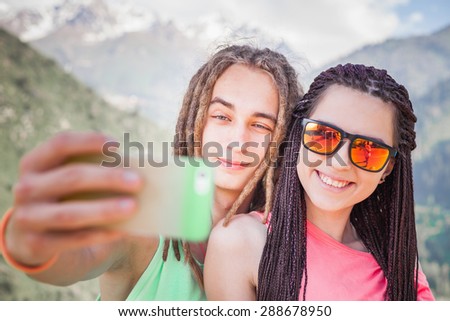 Happy and funny people make selfie or make pictures of themselves on mobile phone at mountain outdoor. They dressed at hipster style clothing, sunglasses, has long hair