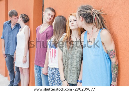 Medium group of young people kissing and standing in row near red wall background. They celebrate a holiday of International, World Kissing Day 6 July or Valentine\'s Day