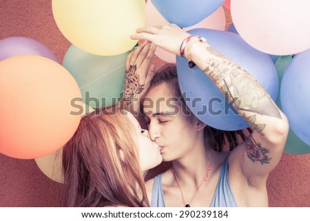 Closeup funny young couple kissing at background of color balloons. They celebrate a happy birthday or summer holiday! Like an International, World Kissing Day 6 July or Valentine\'s Day