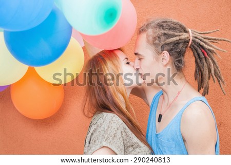 Happy and funny young couple kissing at background of color balloons. They celebrate a birthday or some International holiday! World Kissing Day, Valentine\'s Day, with copy space for any text, design