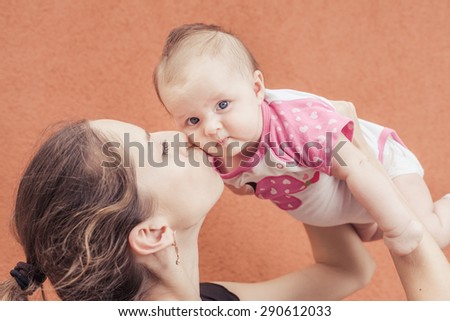 Happy mother kissing her baby at wall background. Baby looking at camera. Mothercare is most important in baby life. Image ready for International Kissing Day or World Kiss Day