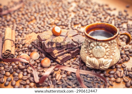 For holiday of chocolate day - wooden table background decorated a lot of coffee beans, chocolate bar, a cup of hot coffee, cacao, nuts, cinnamon. Selective Focus at nut