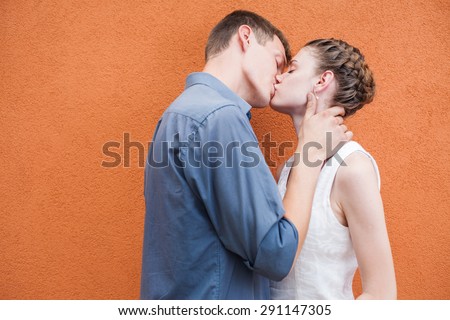 Kissing young couple at red wall background. Image ready for International, World Kissing Day 6 July or Valentine\'s Day, with copy space for any text or design