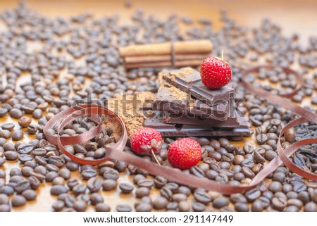 For holiday of chocolate day - wooden table background decorated a lot of coffee beans, chocolate bar, cacao, strawberries, cinnamon. Selective focus