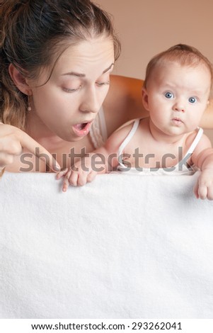Mother and baby lying on a white blanket. Advertising banner sign - Mom is pointing down and baby looking down on empty blank billboard or sign board. There is a copy space for text and design