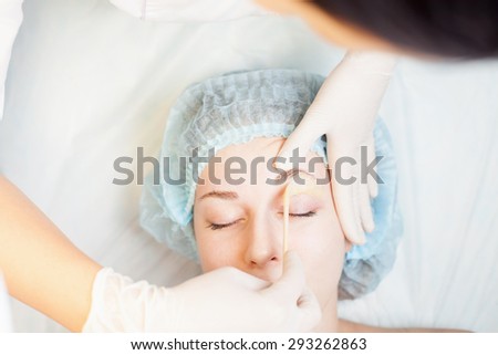 Professional woman at spa beauty salon doing epilation or correction eyebrow using sugar  - sugaring. You can see her smooth eyebrow after hair removal