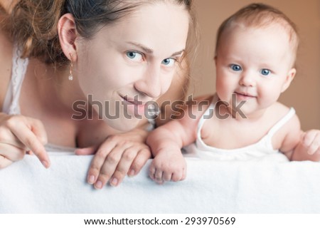 Happy mother and baby lying on a white blanket. Advertising banner sign - Mom is pointing down and surprised baby looking at camera.