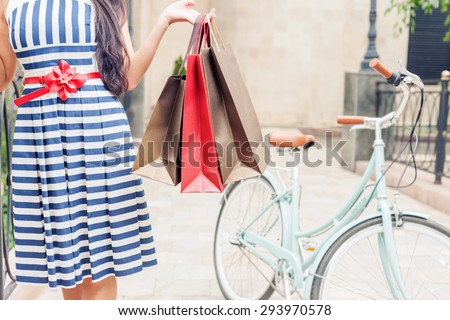 Closeup fashion woman dressed in striped dress with bags and vintage bike has shopping travel to Italy, Milan. She has happy vacation travel to Europe