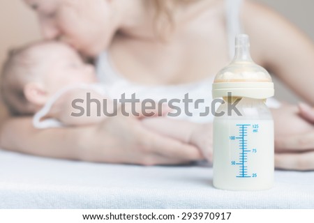 Baby bottle with breast milk for breastfeeding at foreground and mother with baby at background, mothers breast milk is the most healthy food for newborn baby