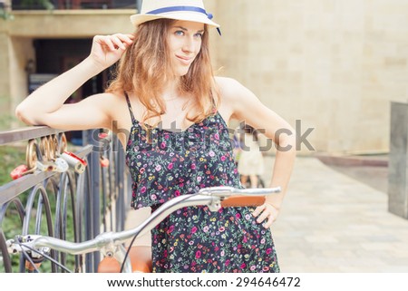 Fashion woman travel at europe by city vintage bicycle at summer time, she is dressed in elegant dress and standing on bridge at background. Selective Focus at girl