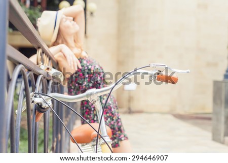 beautiful woman travel at europe by city vintage bicycle at summer time, she is dressed in elegant dress and standing on bridge at background. Selective Focus at bicycle handle at foreground