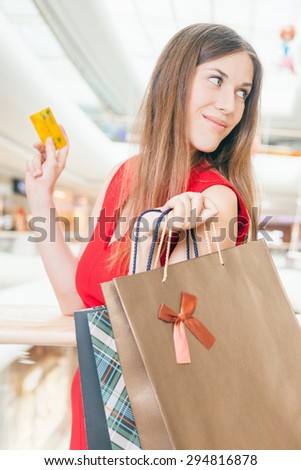 Concept of shopping and payment by plastic card at big mall center. Fashion successful woman holding credit card and bags with purchases. She is happy and awesome buyer!