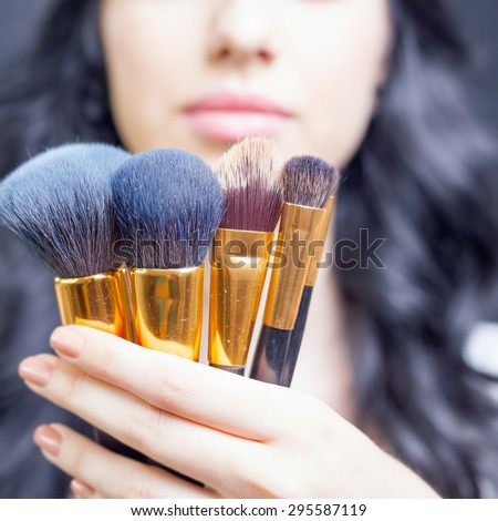 Closeup beautiful woman Arab appearance in the beauty salon with a nice makeup. Holding in hands a set of professional makeup brushes on a dark or black background.