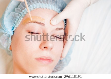 Beautiful woman in spa salon receiving epilation or correction eyebrow using sugar  - sugaring. You can see her smooth eyebrow after hair removal