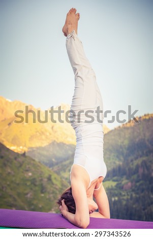 Young asian woman doing yoga at mountain, dressed in white sportswear. She standing on two hands