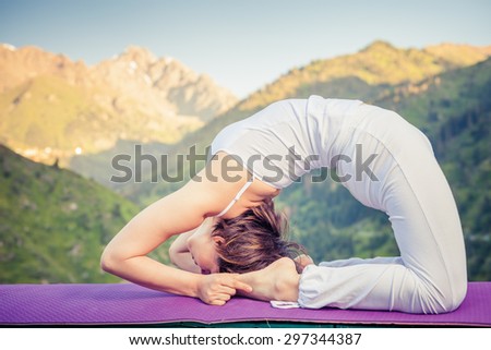 Young asian woman doing yoga at mountain, dressed in white sportswear. She standing on two hands like bridge pose.