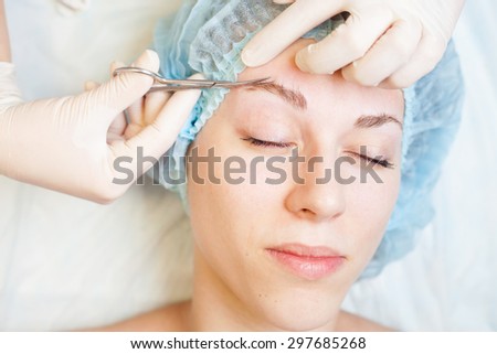 Professional woman at spa beauty salon doing correction and cuts eyebrow using nail scissors. You can see her smooth eyebrow after hair removal