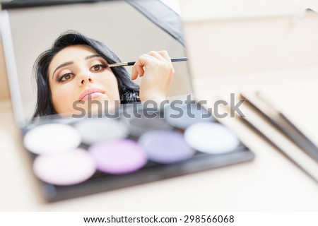 makeup artist woman doing make-up using cosmetic brush and mirror applying eye shadow on the eyelids for yourself at beauty salon with white background