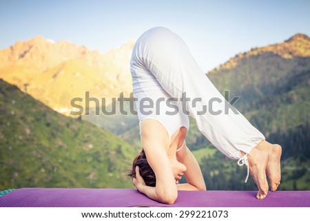 Young asian woman doing yoga at mountain, dressed in white sportswear. She standing on two hands