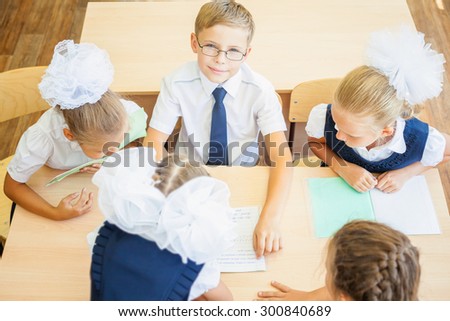 Group of schoolchildren or kids at school classroom sitting at a desk and help each other with their homework. Boy looking at the camera. Concept of teamwork among students